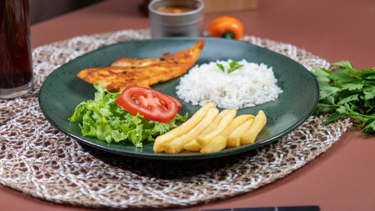 Appetizing meal featuring grilled fish, rice, and fries with fresh salad on a woven mat.